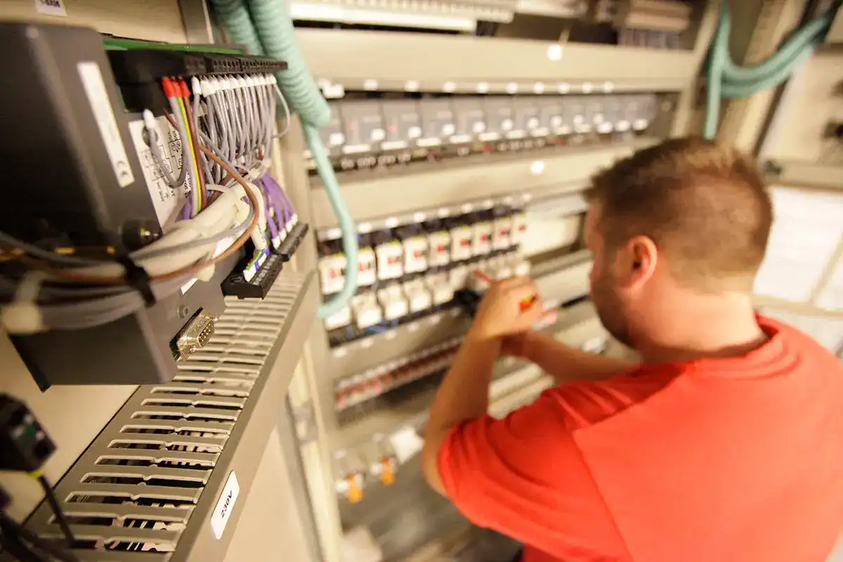 en mann i rød skjorte jobber på et elektrisk panel.